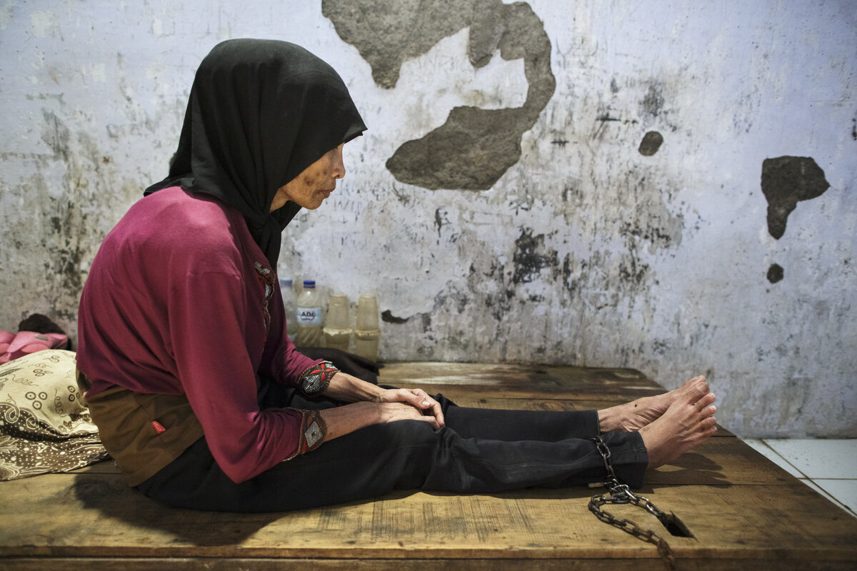 A young woman with a real or perceived psychosocial disability sits with her ankle chained to a platform bed at Bina Lestari faith healing center in Brebes, Central Java. Photo: © 2018 Andrea Star Reese
